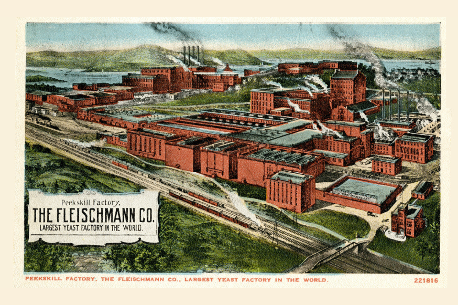 Image of a postcard featuring the Fleischmann Factory in the background. Foreground features two trains. Text reads “Peekskill Factory, The Fleischmann Co. Largest Yeast Factory in the World” Text underneath reads the same and number code 221816